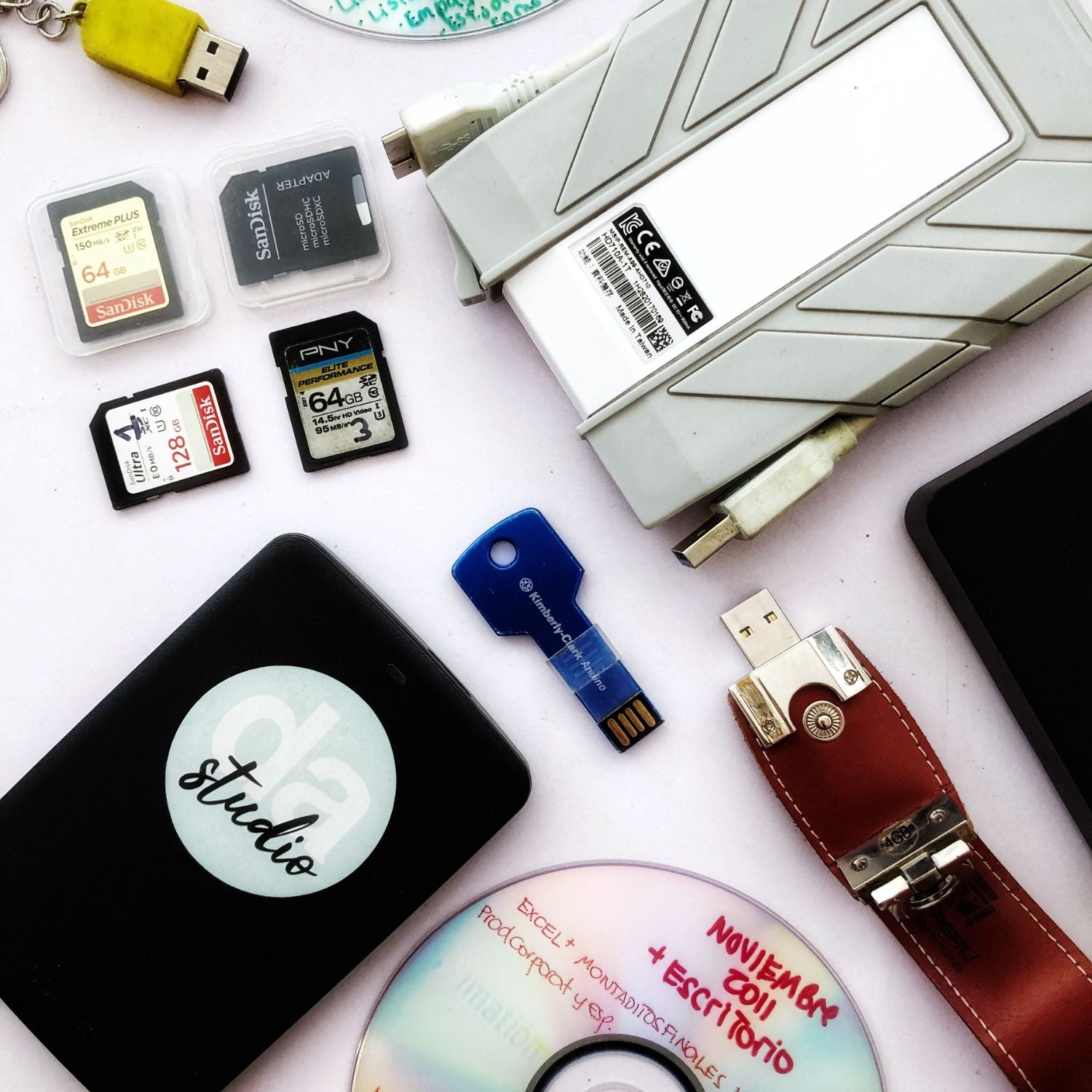 Bastantes tarjetas de memoria, un disco, un usb y un disco duro externo sobre una mesa.
