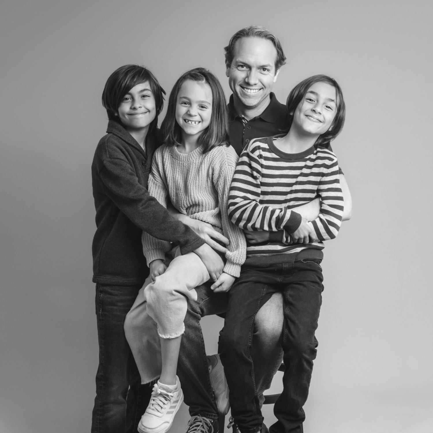 Familia sonríe a la cámara frente a un fondo de fotografía.